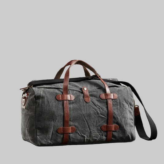 Gray duffel bag with brown leather straps on a dark wooden surface