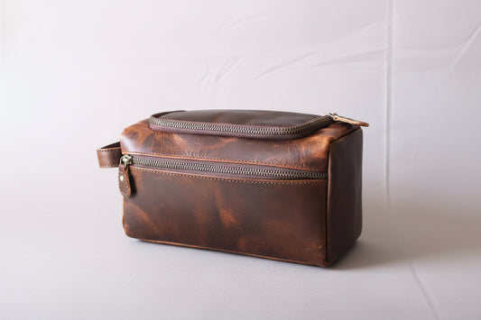 Brown leather toiletry bag with zippers on a black surface