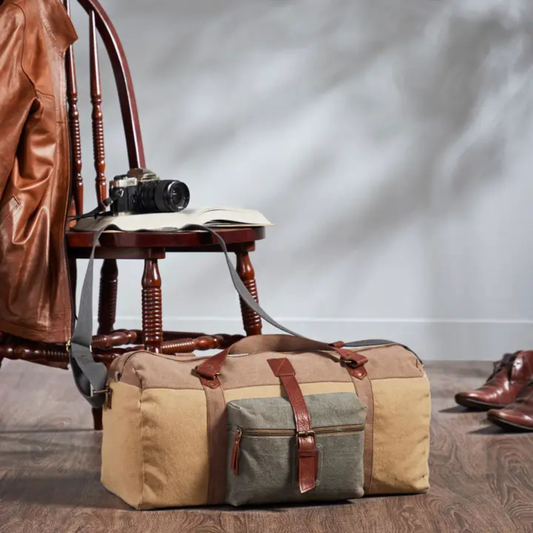 Multicolored duffel bag with leather straps on a wooden floor next to a chair and shoes.