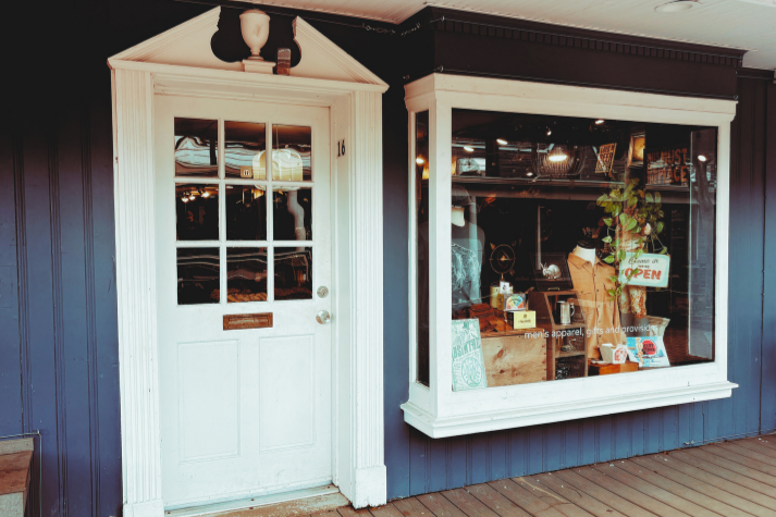 Storefront with a white door and display window against a blue wall.
